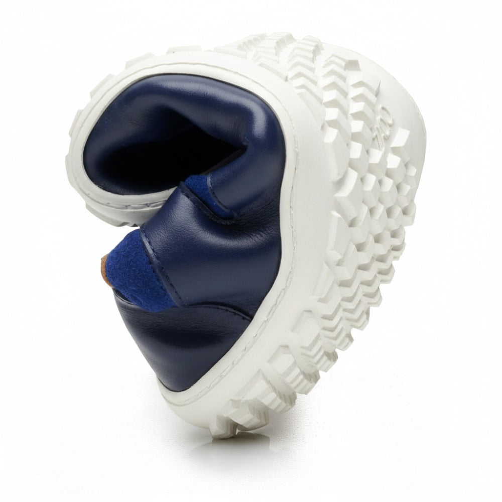 Das Bild zeigt eine Nahaufnahme des SHOQQ Trident von ZAQQ, der ein marineblaues und weißes Design mit einer klobigen, strukturierten Sohle aus robustem Kautschuk aufweist, die gedreht ist, um seine Flexibilität hervorzuheben. Das Obermaterial des Schuhs ist glatt und aus nappalederähnlichem Material gefertigt, was einen idealen Kontrast zur robusten Sohle bildet.