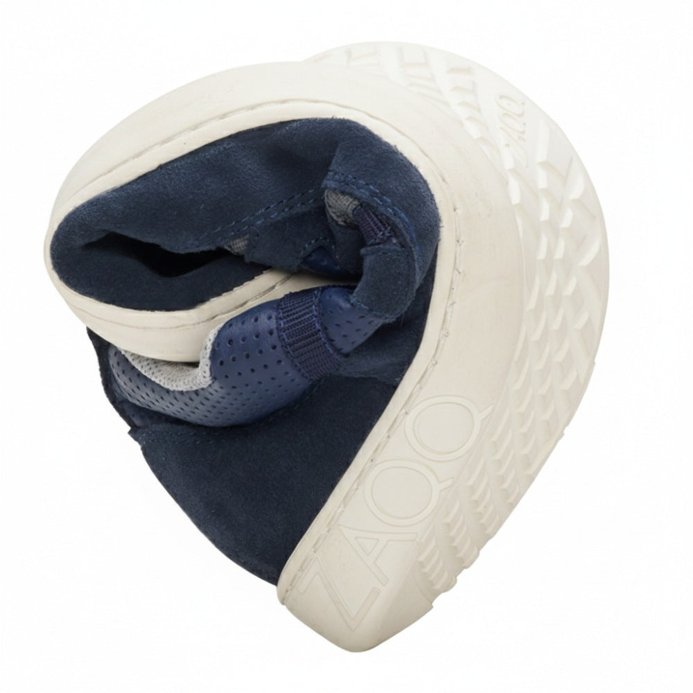 Ein gefalteter DRAQE Azul Sneaker in Weiß und Marineblau zeigt das ZOO-Logo auf der Außensohle. Dieser von ZAQQ aus Nappaleder gefertigte Schuh bietet außergewöhnlichen Komfort. Seine profilierte Sohle verbessert Flexibilität und Kompaktheit.