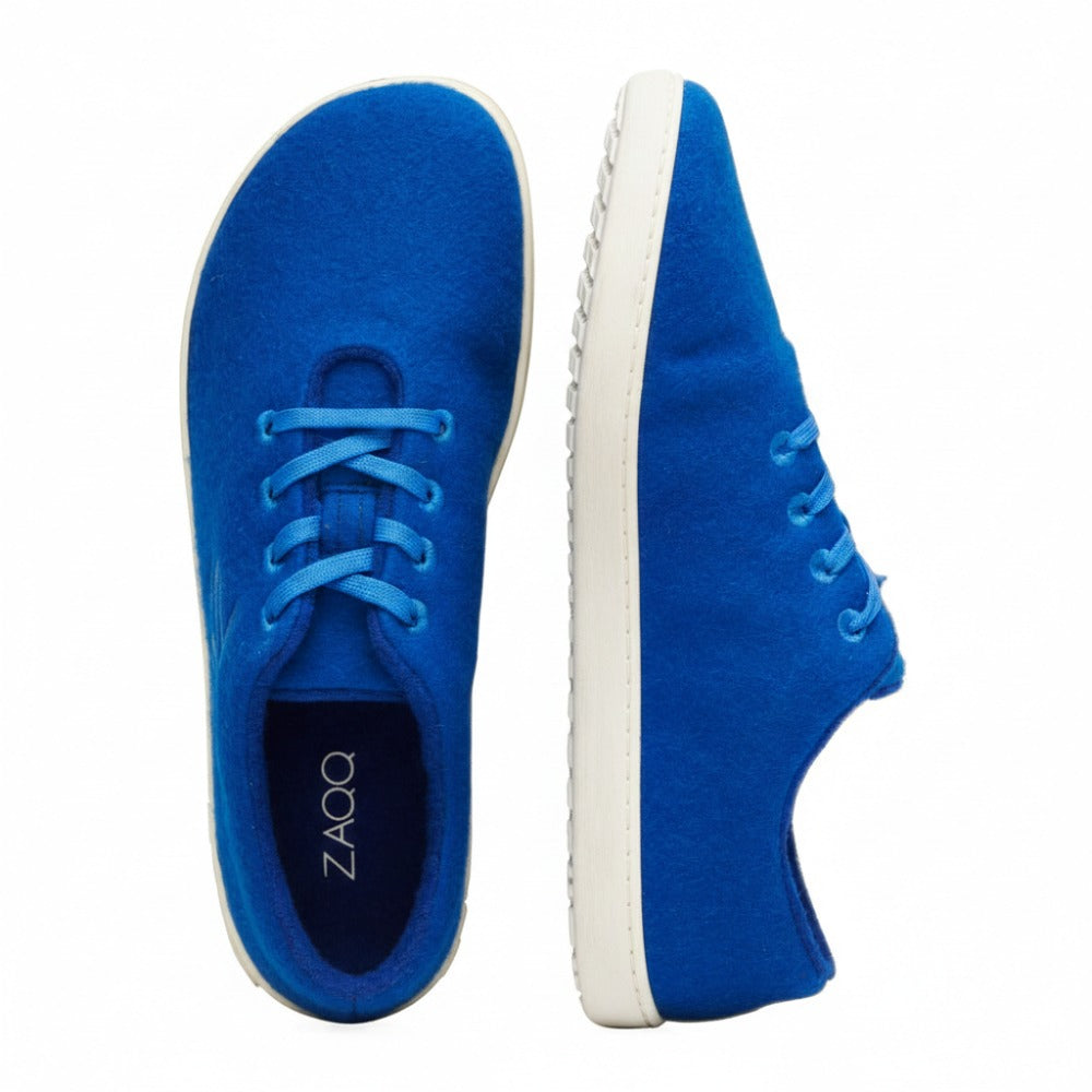 Ein attraktives Paar LIQE Azur-Sneaker von ZAQQ aus Merinowolle zeigt eine leuchtend blaue Farbe, wobei ein Schuh von der Seite und der andere von oben zu sehen ist. Diese Schuhe haben weiße Sohlen und blaue Schnürsenkel, während die Innensohle des oberen Schuhs stolz ihr Branding als einzigartiger Barfußschuh zeigt.