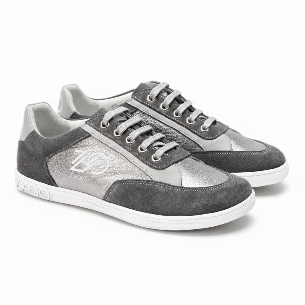 Et par OQTAV Grey-sneakers fra ZAQQ, laget av fløyelsmykt semsket skinn og strukturerte innsatser. Med sølvfargede lisser og den karakteristiske Zagoo-logoen på siden og hælen, presenteres disse stilige skoene side om side på en hvit bakgrunn.