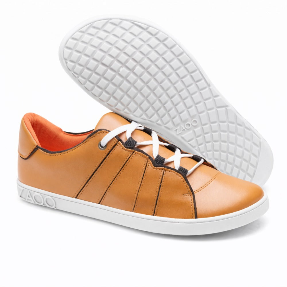 Ein Paar stylische QQQ Low Sierra Sneaker von ZAQQ, in braunem Nappaleder-Design mit weißen Schnürsenkeln und flexibler Kautschuksohle. Ein Schuh steht aufrecht, während der andere geneigt ist, um seine strukturierte Sohle hervorzuheben. Der Markenname ZAQQ ist elegant auf der Seite und der Sohle angebracht.