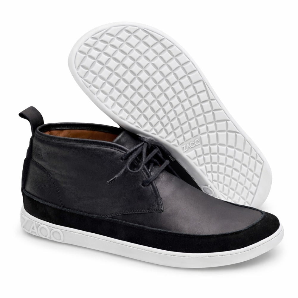 Ein Paar stylische schwarze ZAQQ QUITMAN High-Top-Sneaker mit kontrastierenden weißen Sohlen. Ein Sneaker steht aufrecht und zeigt sowohl das Seiten- als auch das Vorderprofil, während der andere liegt und eine strukturierte Sohle mit dem ZAQQ-Branding hervorhebt.