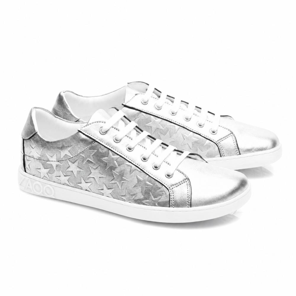 SLOQ Stars Silver-sneakers fra ZAQQ har hvite lisser og stjernemønster på sidene, supplert med en hvit såle med VAOO-preget på hælen. Disse skoene kjennetegnes av et slankt og moderne design med en skinnende metallisk finish.