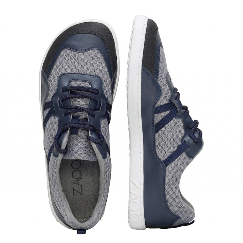 Wir präsentieren die ZAQQ SQATE Grey Sportschuhe – ein Paar graue und marineblaue Sneaker, ideal für jeden aktiven Tag. Diese Damen-Sneaker verfügen über ein atmungsaktives Netzmuster, weiße Sohlen und dunkelblaue Schnürsenkel. Ein Schuh steht aufrecht, der andere zeigt sein schlankes Seitenprofil und kombiniert so Stil mit Komfort.