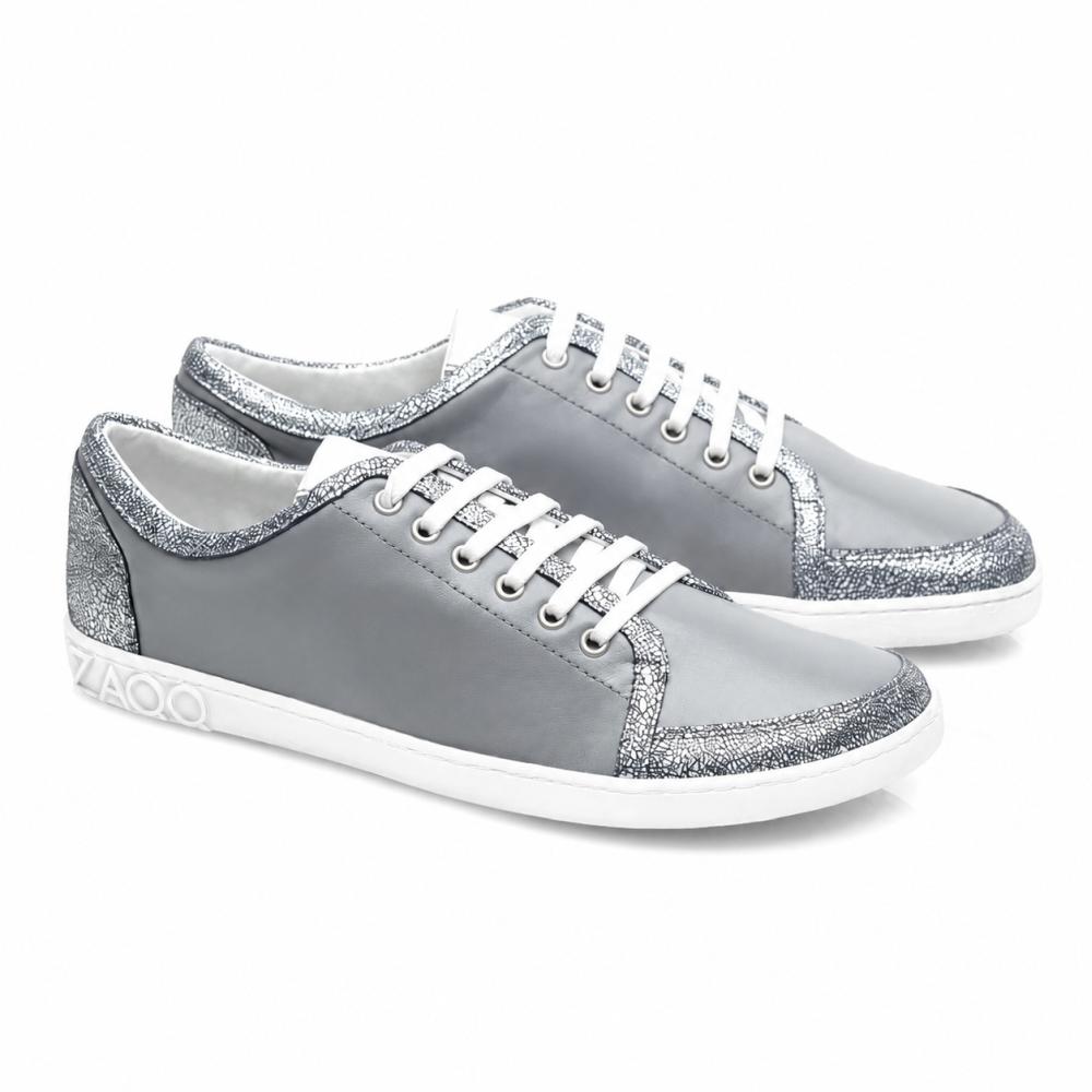 TIQQ Grey Silver Sneaker fra ZAQQ imponerer med sitt enkle design av mykt nappaskinn med hvite skolisser og sølvglitterdetaljer, supplert med hvite såler og en diskret logo på hælen, og tilbyr den perfekte blandingen av stil og komfort for enhver anledning.